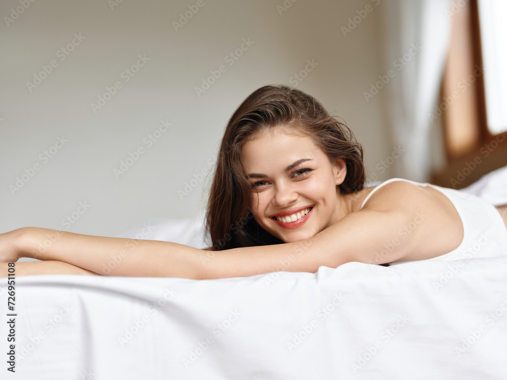 Young sexy woman in brunette lingerie lying in a white bed in the morning on a day off and smiling, vacation lifestyle, home waking atmosphere with sunlight from the window. Young sexy woman in brunette lingerie lying in a white bed in the morning on a day off and smiling, vacation lifestyle, home waking atmosphere with sunlight from the window.