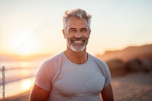 Portrait of a smiling senior man standing on the beach at sunset