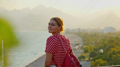Stunnig 4K video of a white ginger girl standing  and looking to the beautiful view of the beach and mountains in the background. The video was made on a summer day in sunset (sunrise). photo