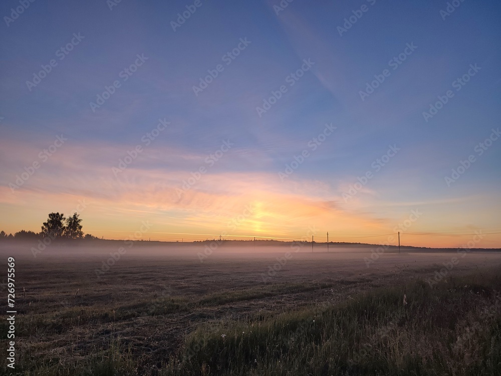 Sunrise at dawn early in the morning in a field covered with fog against a beautiful sky