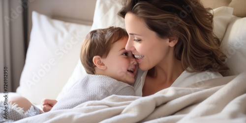 Mother and her young child, snuggled up and smiling in a bright, cozy bed
