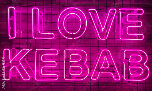 Neon shining sign in pink or purple color on a brick wall with the inscription or slogan I love kebab. Brick wall, background. Bright electric neon light. Cafe-restaurant Doner Kebab.