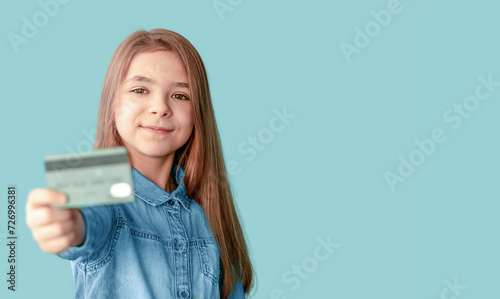A girl in a denim shirt holds a credit card in her hands isolated on a blue background. Copy space photo