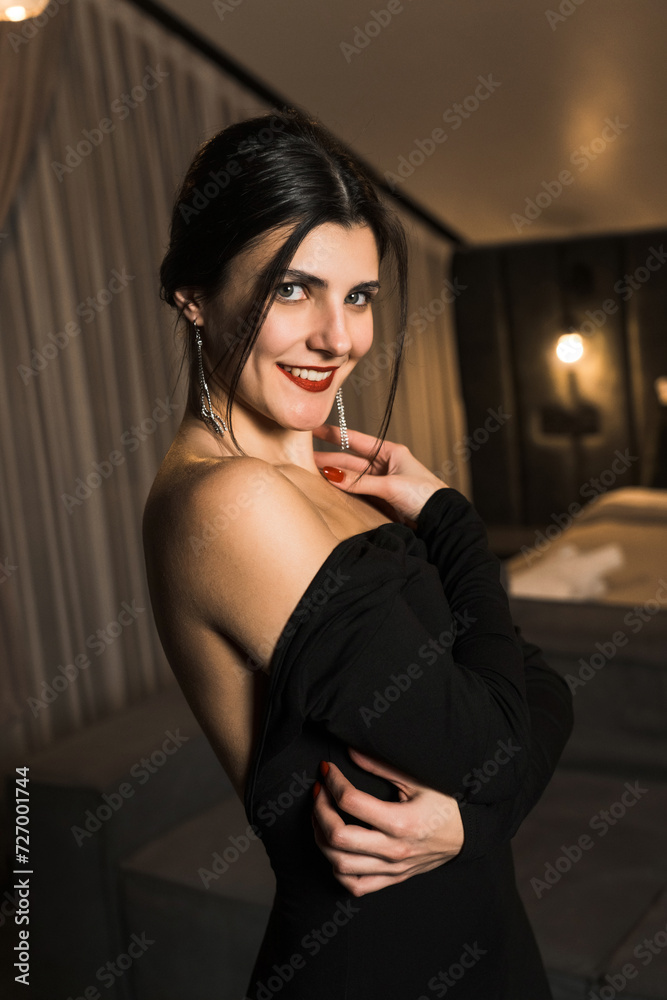 Fototapeta premium Elegant woman in a black dress posing in an apartment. Fashion shooting concept