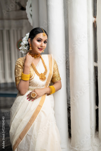 фотографія Stunning bride dressed in a traditional Indian bridal saree with gold jewellery smiles tenderly in front of a vintage background