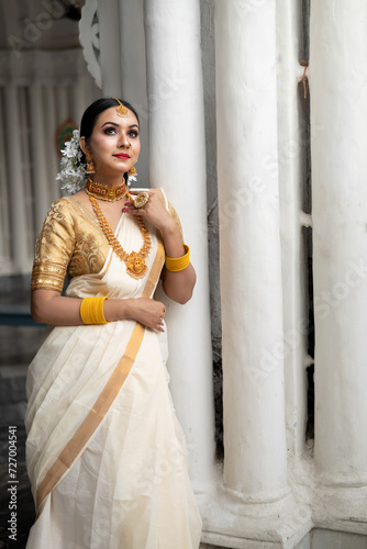 Stunning bride dressed in a traditional Indian bridal saree with gold jewellery smiles tenderly in front of a vintage background. Wedding fashion and lifestyle.
