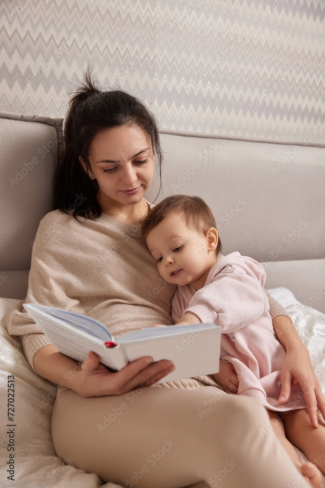 beautiful mother reading book to her cute little daughter on bed beautiful mother reading book to her cute little daughter on bed
