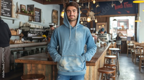 In a bohemian coffeehouse, a laid-back male model wears a faded denim blue hoodie, the relaxed fit and vintage color capturing the eclectic spirit of the venue, mockup