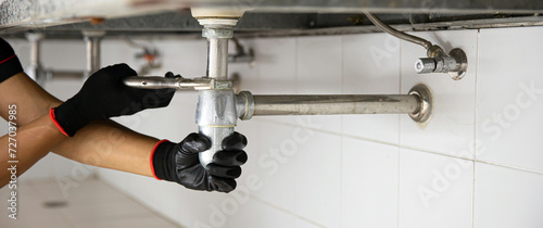 Technician plumber using a wrench to repair a water pipe under the sink. Concept of maintenance, fix water plumbing leaks, replace the kitchen sink drain, cleaning clogged pipes is dirty or rusty. photo