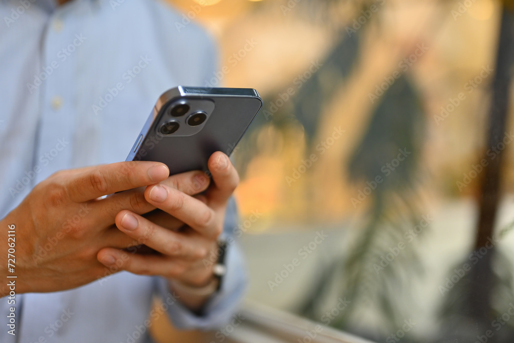 Close-up with an unrecognizable businessman using a smartphone beside window