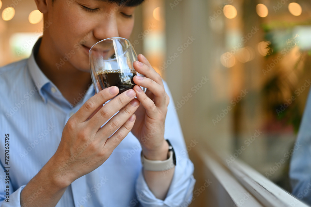 Cropped image with smart looking Young Asian man feeling refreshed by drinking and smelling a cup of coffee