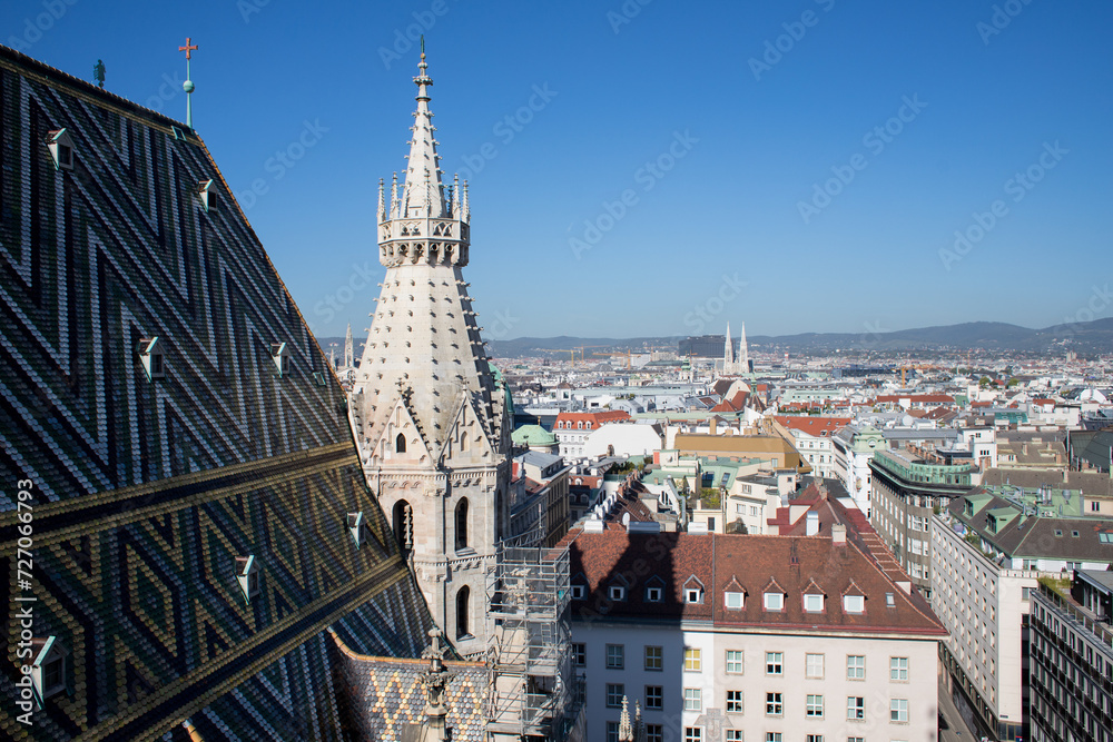 The high spire of the church is in the Gothic style. High dome of gray color in cat style. Panorama of the capital of Austria, Vienna. Stylish colored roof tiles.