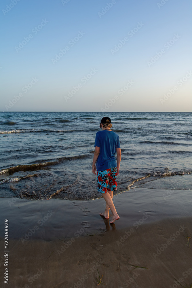 A boy from behind on a sandy beach by the sea