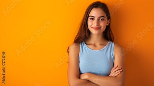 A self-assured, stunning woman, dressed in a vibrant blue singlet, stands tall with her arms crossed against a captivating backdrop of orange. Her confident demeanor exudes charisma. Ideal f