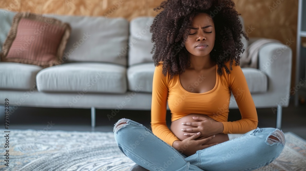 Black lady suffering from menstrual pain, feeling sick to her stomach, touching belly, having abdominal cramps during period, sitting on floor near couch at home Black lady suffering from menstrual pain, feeling sick to her stomach, touching belly, having abdominal cramps during period, sitting on floor near couch at home