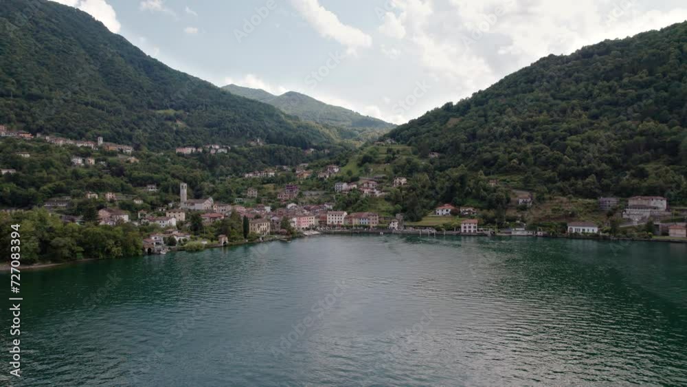Drone flies over the lake and you can see the small fishing village of Osteno in Italy. Breathtaking scenery on a beautiful sunny summer day. Drone flies over the lake and you can see the small fishing village of Osteno in Italy. Breathtaking scenery on a beautiful sunny summer day.