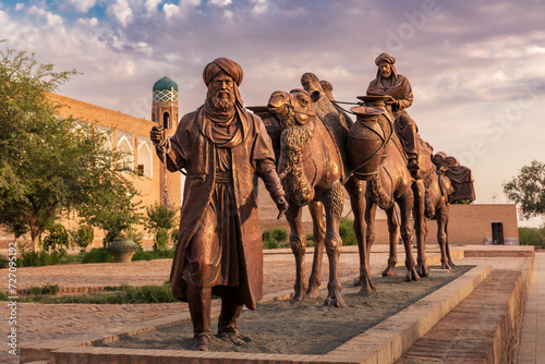 Sculpture of camel carrying goods and man in Uzbek dress in front of city walls, Khiva, Uzbekistan
