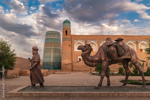 Sculpture of camel carrying goods and man in Uzbek dress in front of city walls, Khiva, Uzbekistan
