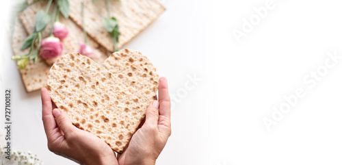 Passover. Person's hands holds Traditional Matzo of heart decorate by pink flowers on white background. banner. top view. Holiday of Jewish people, Spring Holiday. Fasting time