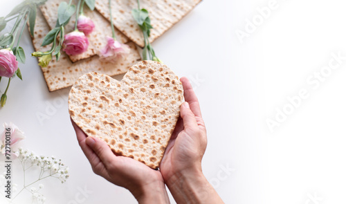 Passover. Person's hands holds Traditional Matzo of heart decorate by pink flowers on white background. top view. Holiday of Jewish people, Spring Holiday. Fasting time