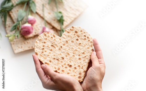 Passover. Person's hands holds Traditional Matzo of heart decorate by pink flowers on white background. banner. top view. Holiday of Jewish people, Spring Holiday. Fasting time