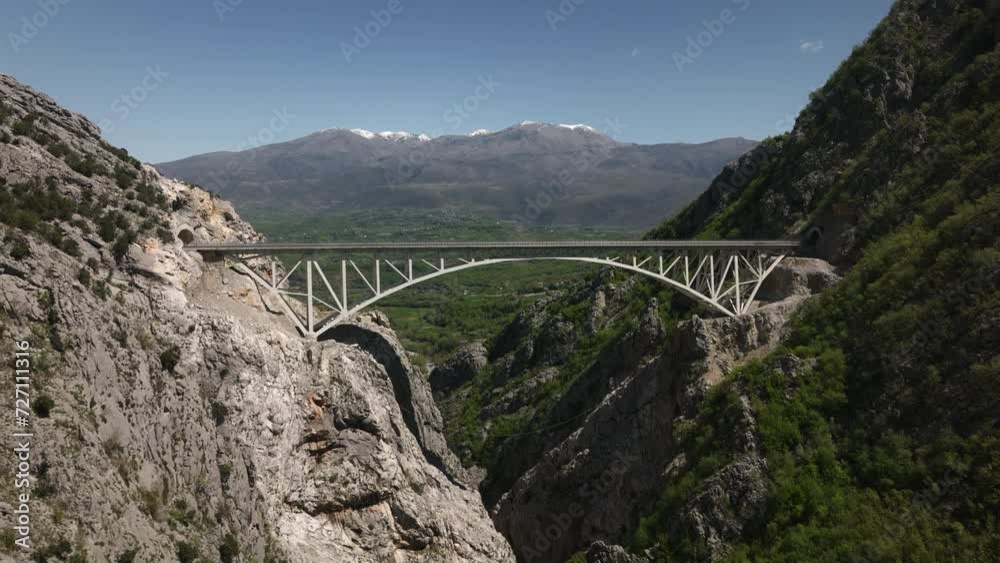 Aerial view of Ura e Lezedrës, Klos - Arbri Road bridge in Albanian mountains, blue sky and snowy summit in the background