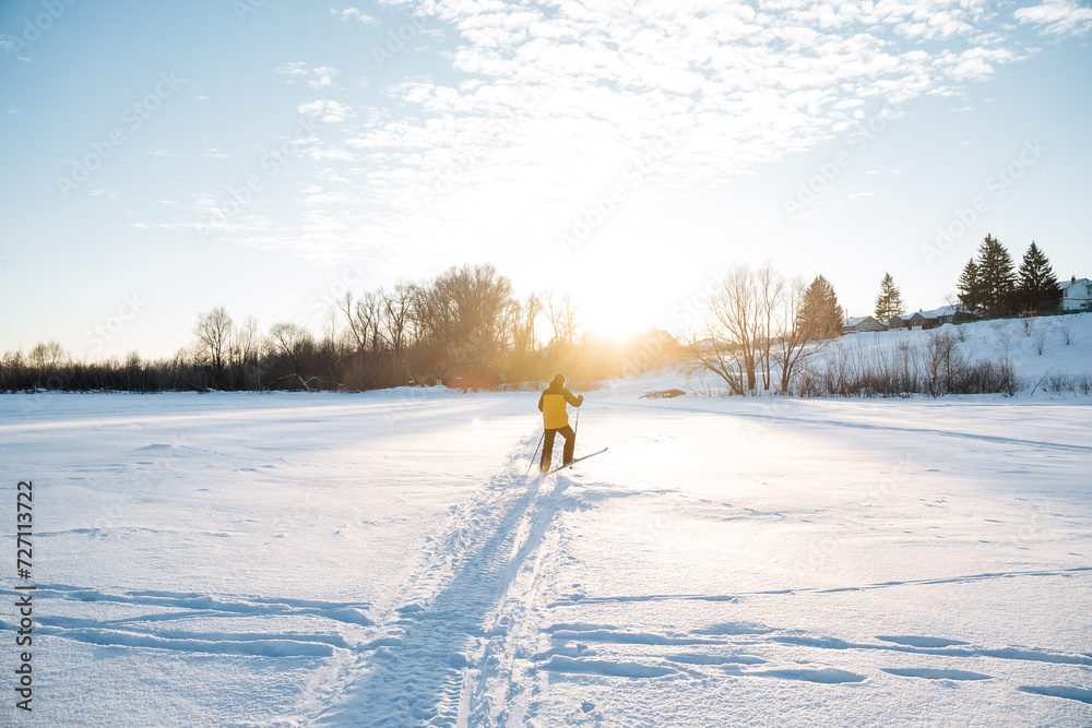 Ski training in the park, skier skiing on a well-trodden path on the lake, sunlight glare into the camera, beautiful winter landscape.