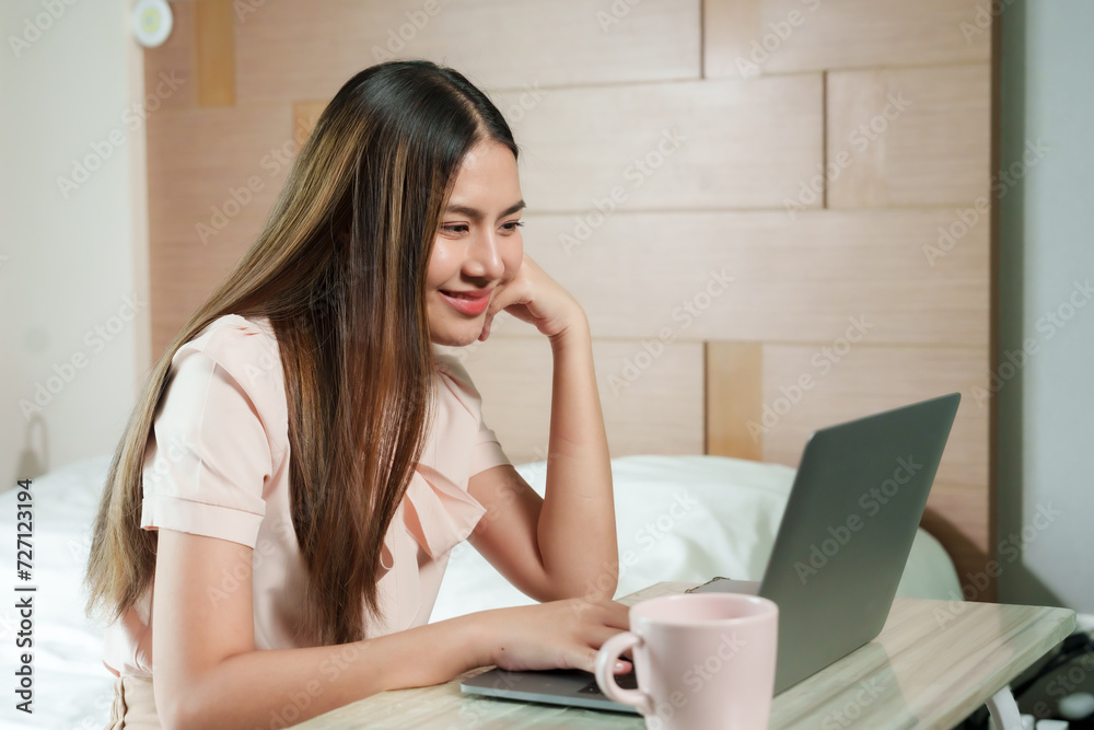 Smiling Asian woman enjoys light moment during work from home, comfortably using her laptop in bedroom. Cheerful and relaxed, professional engages in her remote, reflecting ease in home workspace Smiling Asian woman enjoys light moment during work from home, comfortably using her laptop in bedroom. Cheerful and relaxed, professional engages in her remote, reflecting ease in home workspace