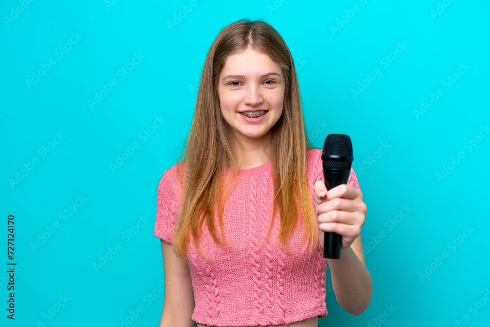 Singer Russian girl picking up a microphone isolated on blue background with happy expression Singer Russian girl picking up a microphone isolated on blue background with happy expression