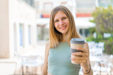 Young blonde woman holding a take away coffee at outdoors with happy expression