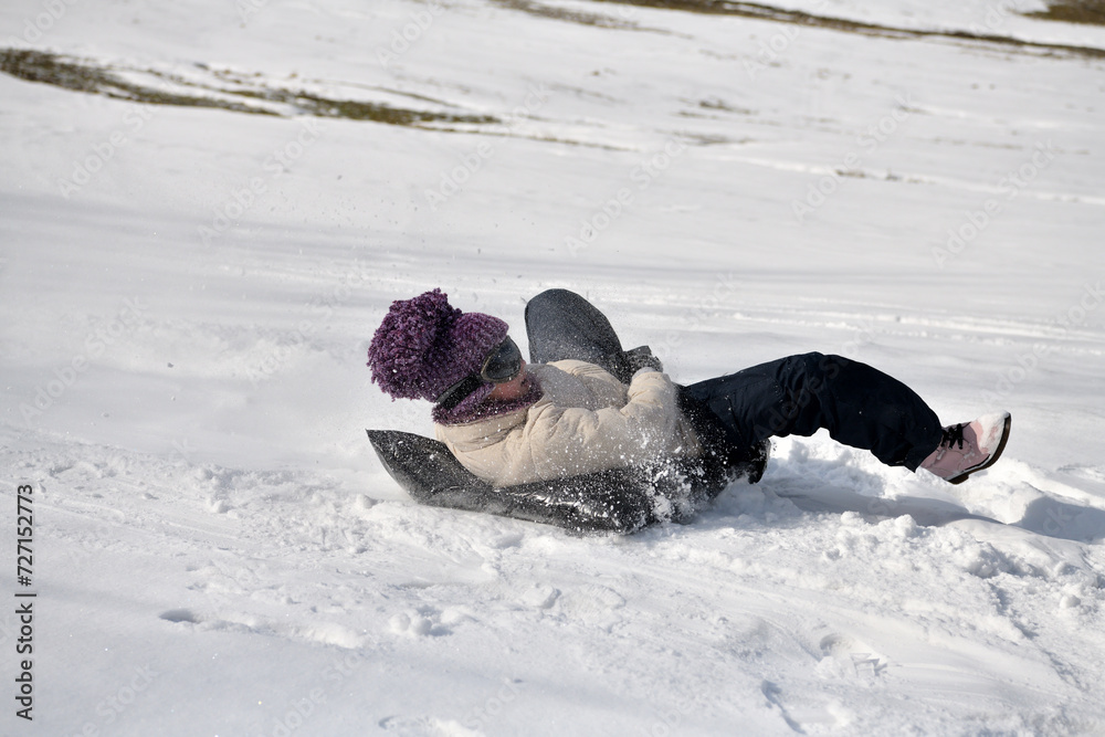 A child slides down a hill in the snow in winter
