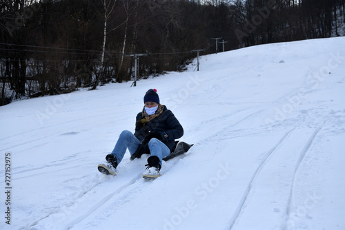 Obraz na płótnie An adult woman sleds down a hill in the winter and brakes with her feet w salonie