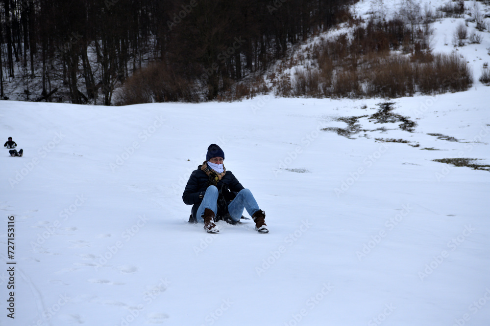An adult woman sleds down a hill in the winter and brakes with her feet