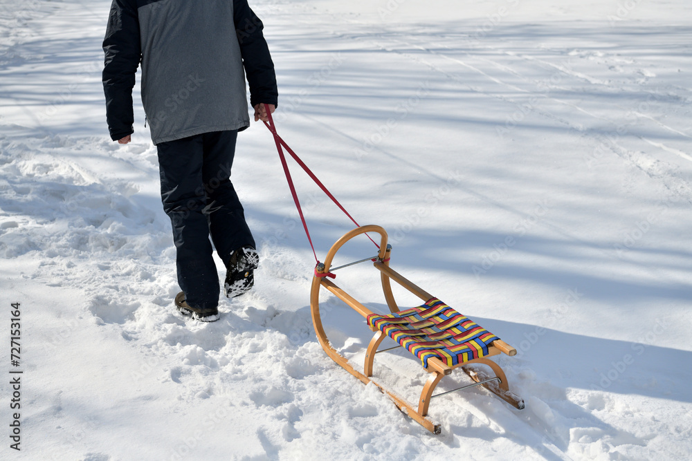 A man pulls a sledge up a hill in the winter tobogganing