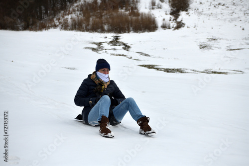 An adult woman sleds down a hill in the winter and brakes with her feet