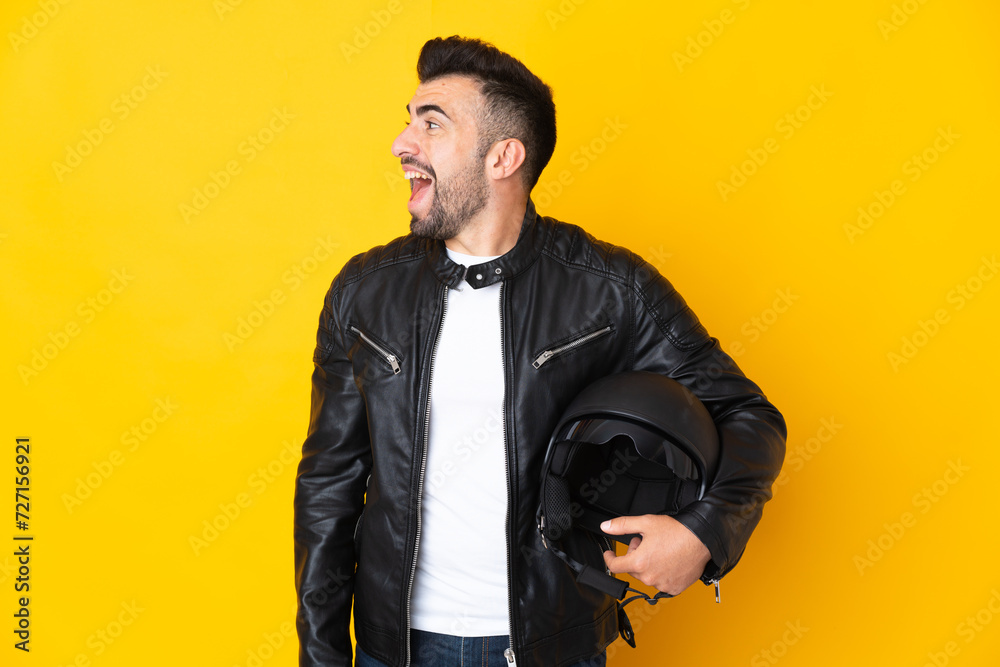 Caucasian man with a motorcycle helmet over isolated yellow background laughing in lateral position Caucasian man with a motorcycle helmet over isolated yellow background laughing in lateral position
