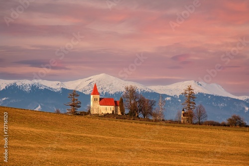 Church on the hill in the early morning. Beautiful sunrise with orange and red tones. In the background, snow-capped mountains. photo