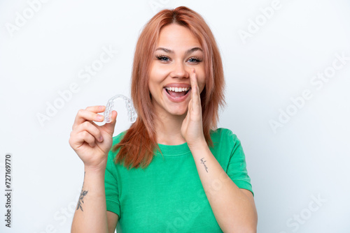Young Russian girl holding invisible braces isolated on white background shouting with mouth wide open