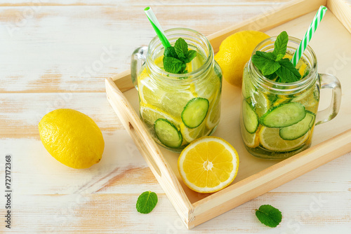 Detox water with sliced lemon and cucumber in a jar on wooden table. Healthy concept.