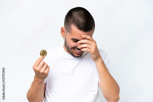 Young caucasian man holding a bitcoin isolated on white background laughing