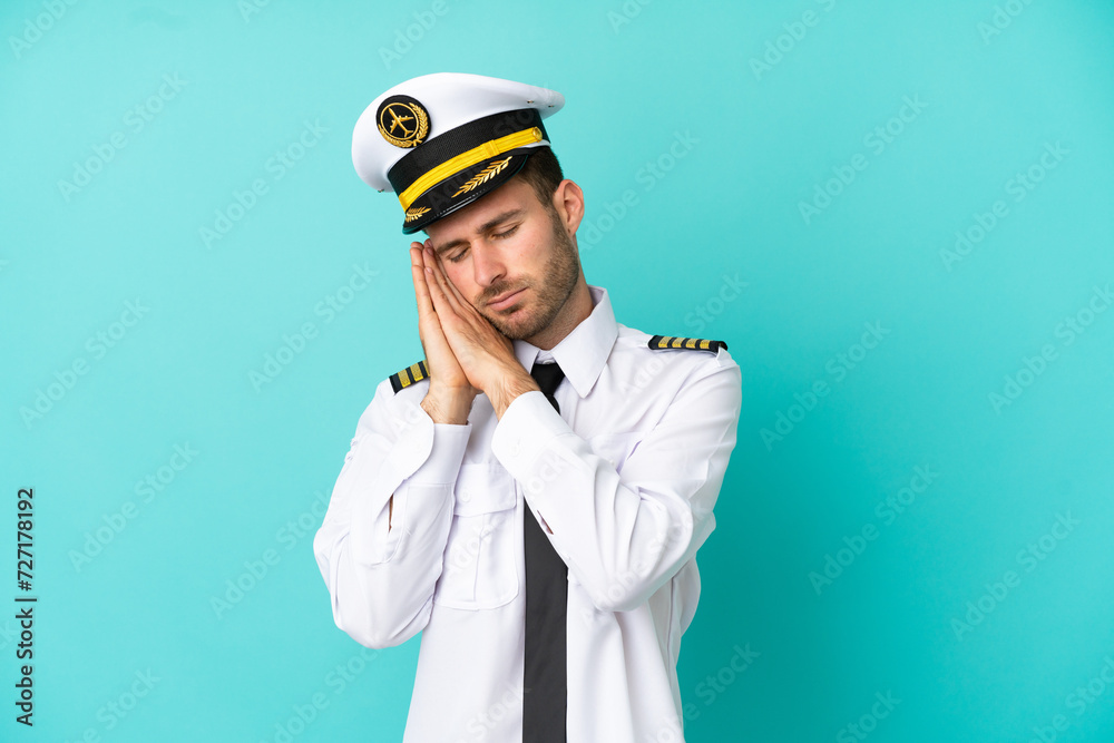 Airplane caucasian pilot isolated on blue background making sleep gesture in dorable expression Airplane caucasian pilot isolated on blue background making sleep gesture in dorable expression