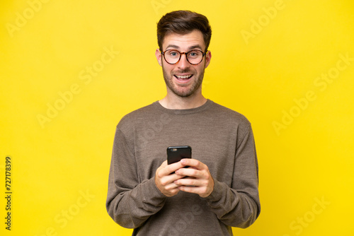 Young caucasian man isolated on yellow background surprised and sending a message © luismolinero