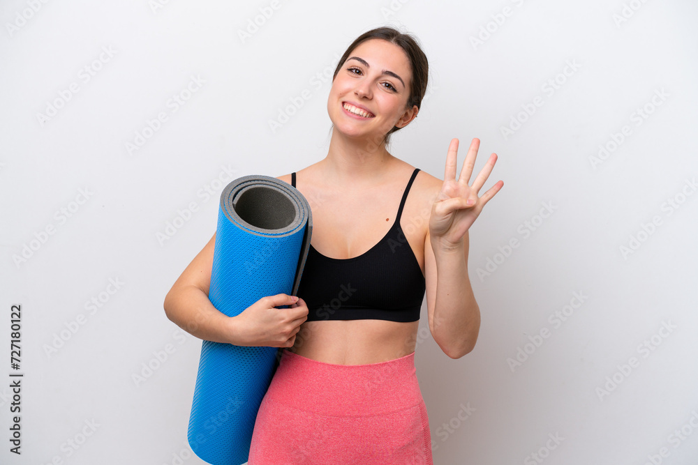 Young sport girl going to yoga classes while holding a mat isolated on white background happy and counting four with fingers