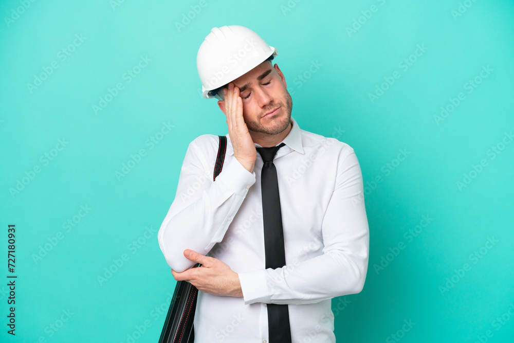 Young architect caucasian man with helmet and holding blueprints isolated on blue background with headache Young architect caucasian man with helmet and holding blueprints isolated on blue background with headache