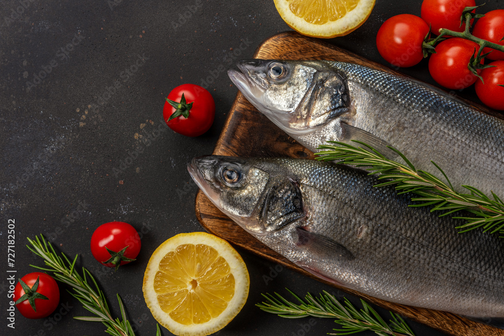 Two fresh seabass fishes with rosemary and vegetables on black table. Two fresh seabass fishes with rosemary and vegetables on black table.