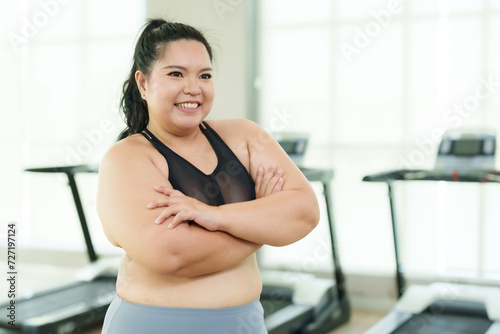 Overweight Asian woman exercise in gym, Cross arms, feeling relaxed and accomplished after workout, with treadmills behind. Content female in sportswear arm stretches, enjoying her fitness