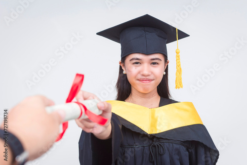 An upbeat female graduate of bachelor of science is handed her diploma while looking at the camera. Full body photo isolated on a white background.