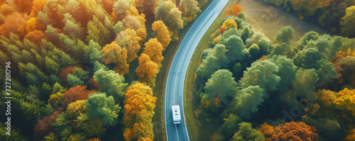 A car drives down a paved road in a mountainous area that cuts through a forest © apirom