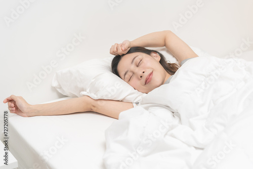 Wake up, beautiful stretching asian young woman waking up after sleep comfortable, rest and relax, closed eyes while with covered blanket, girl stretch in her bedroom,in cozy white bed in the morning.
