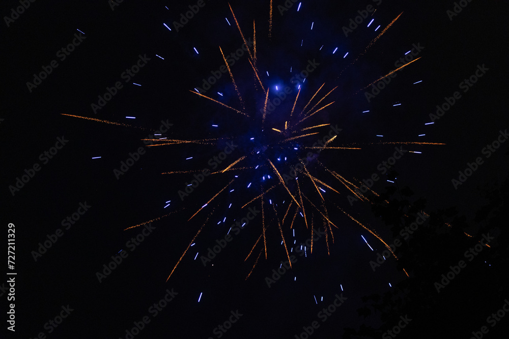 Fototapeta premium Burst of blue and orange fireworks at night - vibrant streaks and sparks - smoke clouds - celebration, new years day, fourth of july, canada day. Taken in Toronto, Canada.